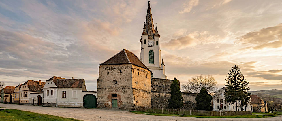 Außenansicht der mittelalterlichen Gräfenburg in Urwegen (Gârbova), Siebenbürgen, eingebettet in ein grünes Hügeltal während der Goldenen Stunde. Der massive Bergfried steht im Zentrum der Ringmauer.