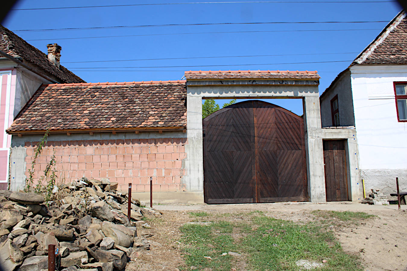 Neu gemauerte Ziegelwand mit historischem Ziegeldach als Rohbau einer Sommerküche neben einem großen Holztor auf einem siebenbürgischen Hof.
