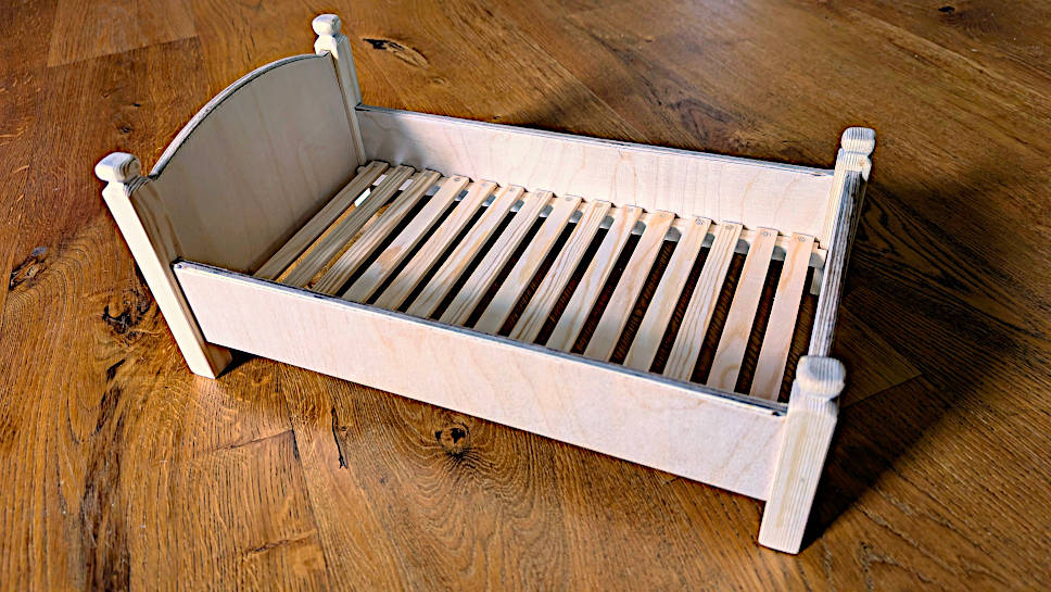Puppenbett selber bauen: Das fertige, metallfreie Holzbett aus Fichte und Multiplex mit detailliertem Lattenrost steht auf einem Holzboden.